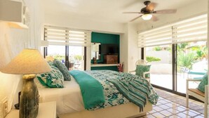 A bedroom with a bed, a ceiling fan, a TV, and a view of the outdoors. - Wrap-Around Patio & Pools · Terrasol Beach Resort (Cabo San Lucas)