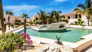 A pool surrounded by palm trees and cacti, with a clear blue sky above. - Wrap-Around Patio & Pools · Terrasol Beach Resort (Cabo San Lucas)