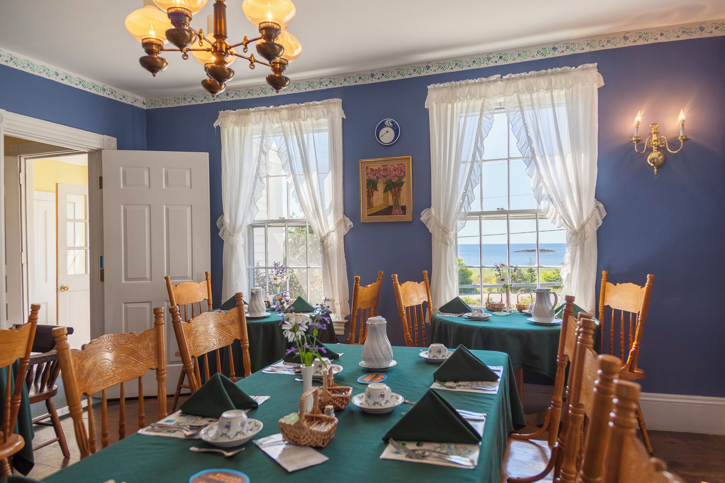 A dining room with a table set for a meal, chairs, a chandelier, and a view through the windows.