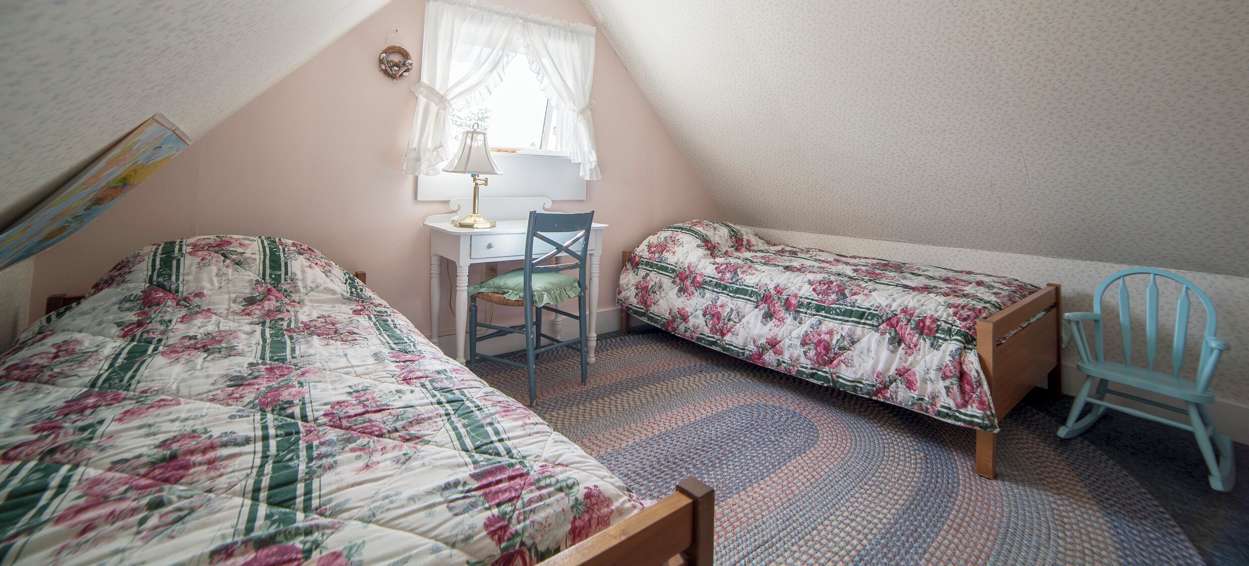 A bedroom with two single beds, a desk, a chair, and a window with curtains.