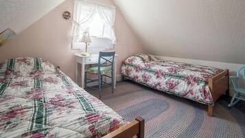 A bedroom with two single beds, a desk, a chair, and a window with curtains.