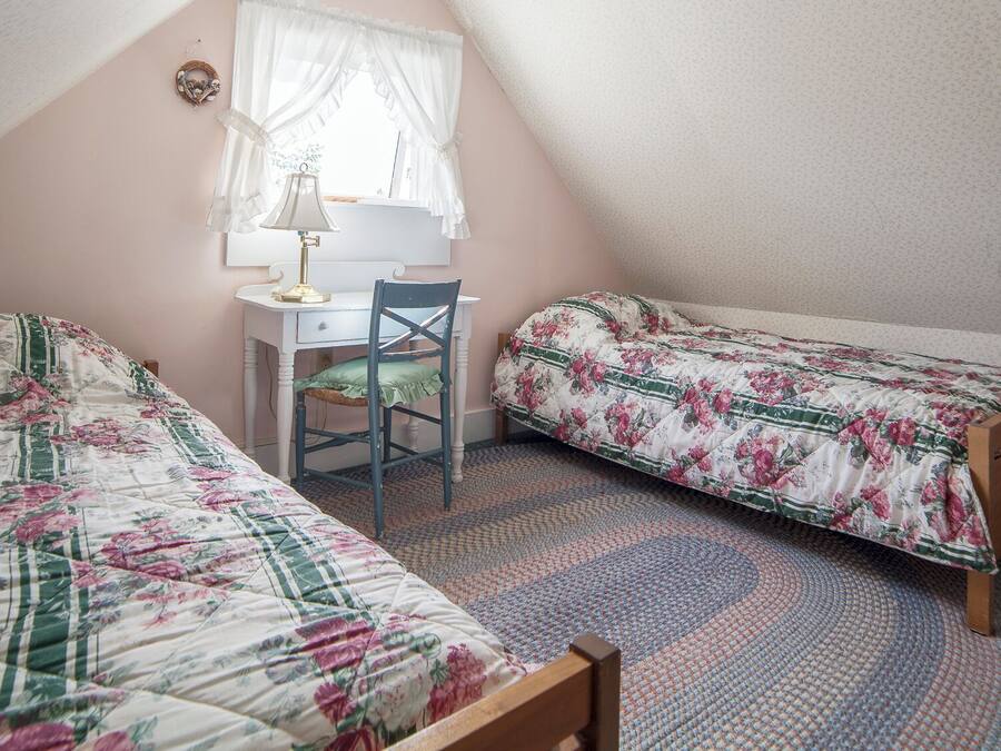 A bedroom with two single beds, a desk, a chair, and a window with curtains.