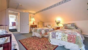 A bedroom with two beds, a sitting area with a chair, a door leading to a balcony, and a decorative border on the ceiling.
