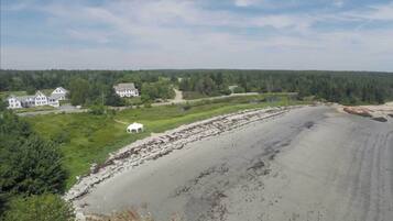 A coastal property with a large sandy beach, a white tent, and a cluster of houses surrounded by dense forest.