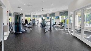A modern gym with various exercise machines, large windows, and a clean, spacious layout.