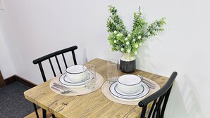 Een eettafel met twee stoelen, een vaas met groene planten, en een kleine potplant aan de muur.
