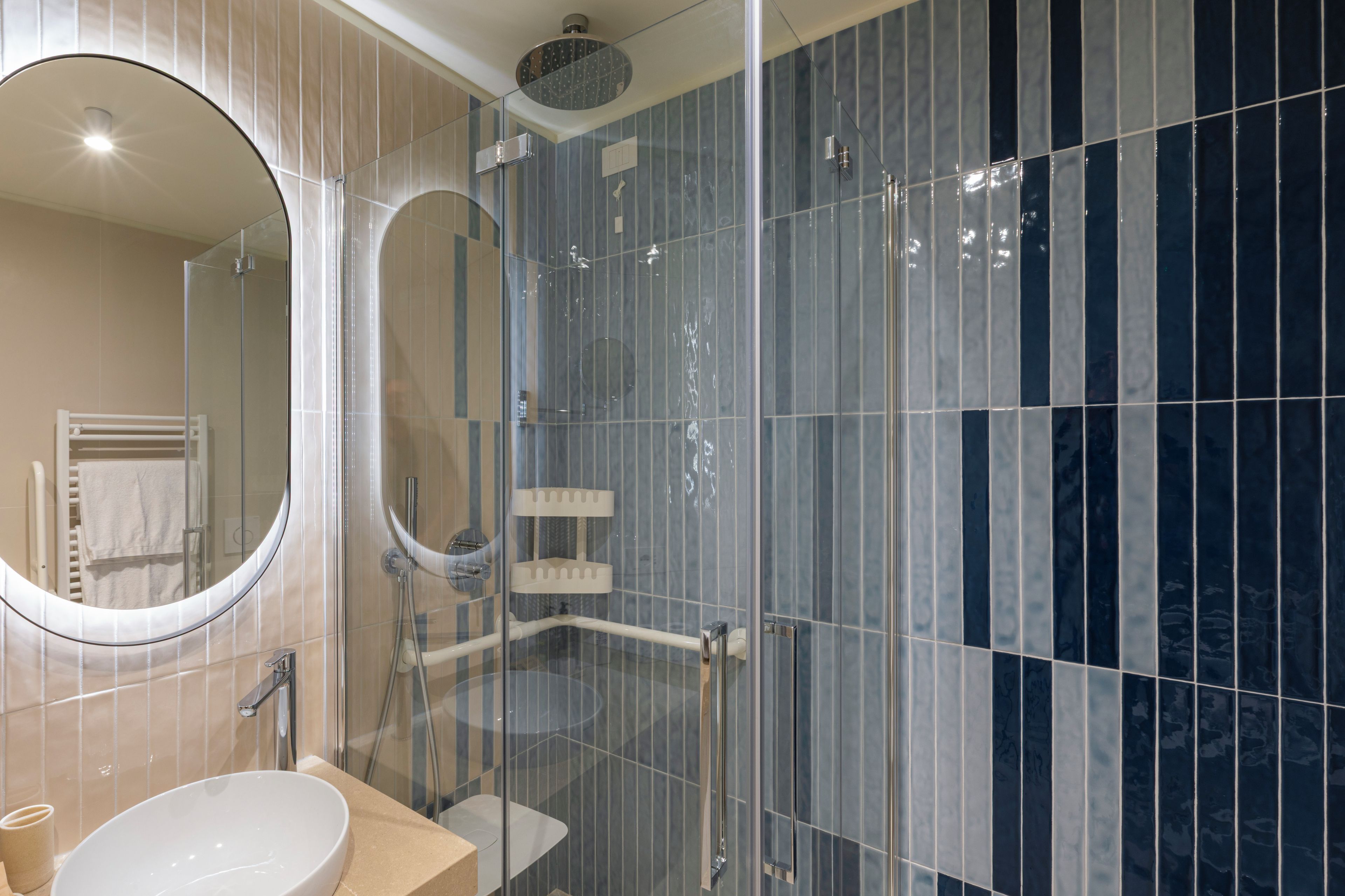 A modern bathroom with a glass-enclosed shower, a round mirror, and a white sink.