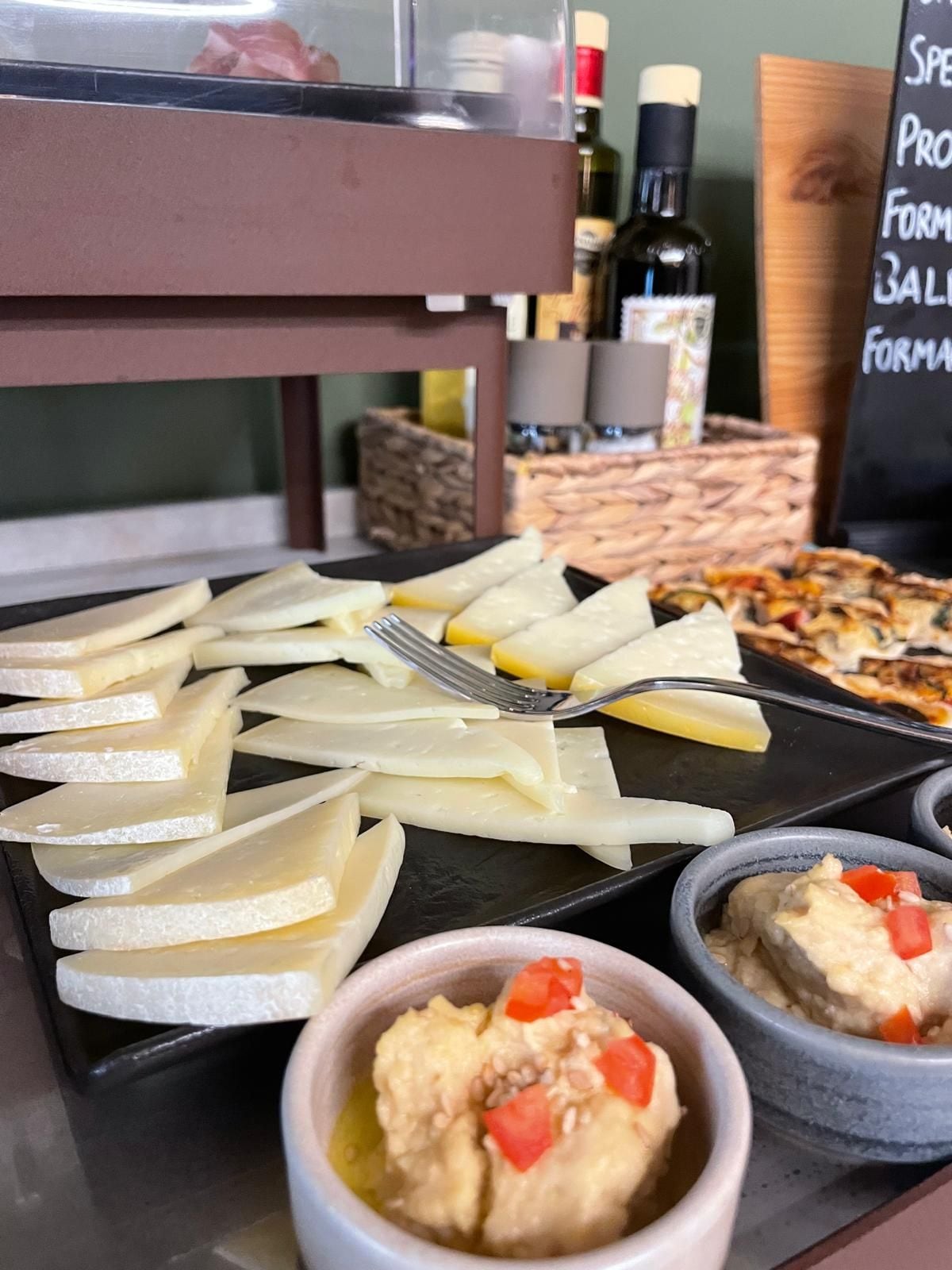 Una mesa de buffet con varios quesos, una pizza y dos fuentes de salsas.