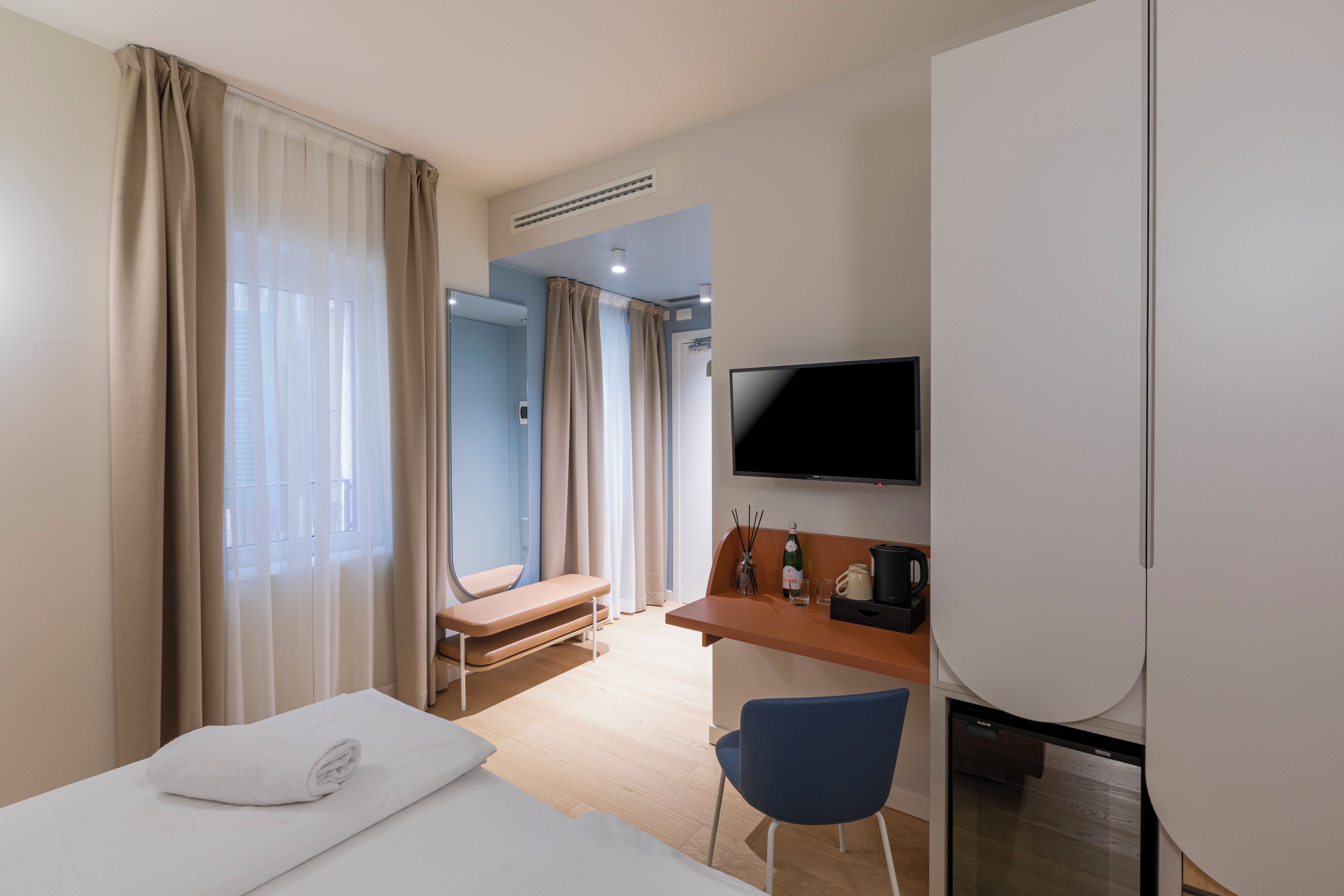 A hotel room with a bed, a desk, a chair, a television, and a bathroom visible through the door.