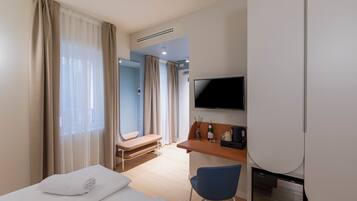 A hotel room with a bed, a desk, a chair, a television, and a bathroom visible through the door.