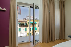 A hotel room with a sliding glass door leading to an outdoor area with a yellow building and green awnings. - Borgo di Lazise (Lazise)