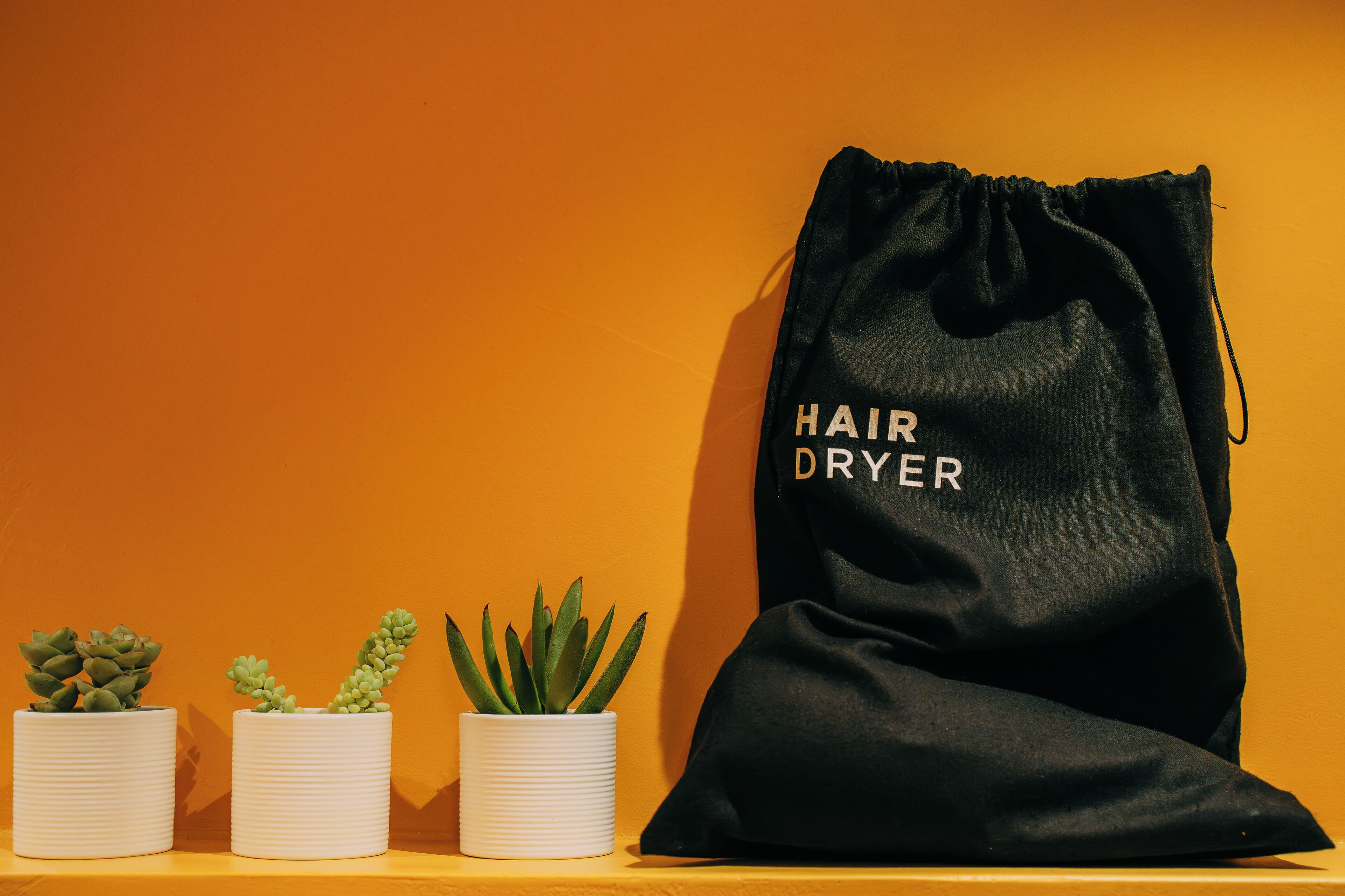 A black drawstring bag labeled "HAIR DRYER" next to three white cylindrical containers with plants.