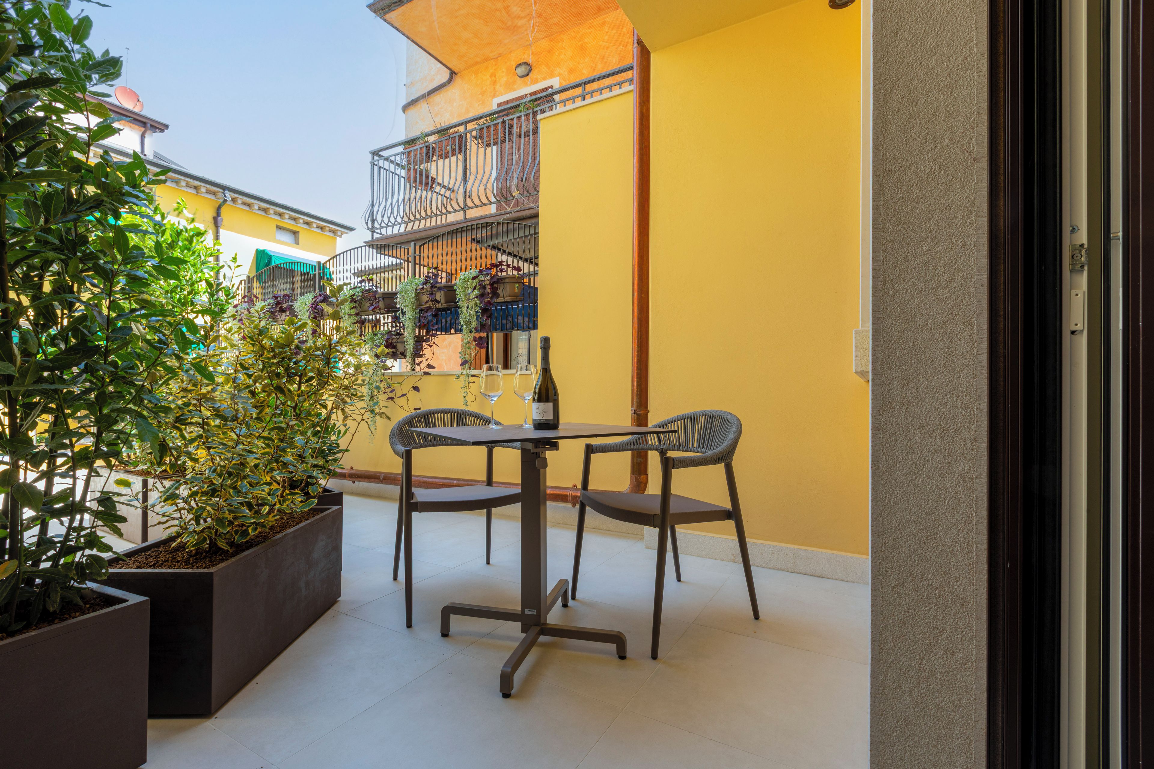 Ein Balkon mit Tisch, Stühlen, Blumentöpfen und einer Weinflasche.