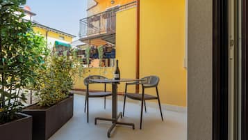 Ein Balkon mit Tisch, Stühlen, Blumentöpfen und einer Weinflasche.