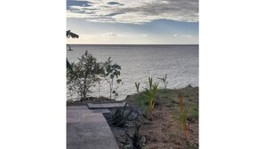 A concrete pathway leading to a body of water, with sparse vegetation and a cloudy sky. - Studio in the Corniche d'or (Pointe-Noire)