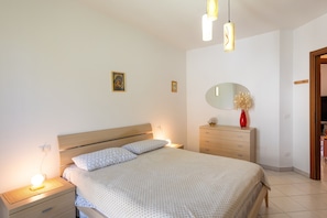 Un dormitorio con cama, mesitas de noche, cómoda, espejo e iluminación en la pared.