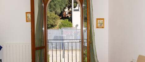 A room with a balcony, a bed, a bedside table, and a window with curtains.