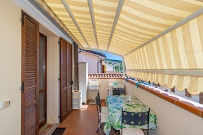 Un espacio al aire libre cubierto con una mesa, sillas y vistas a un edificio de tejado de azulejos.