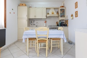Una cocina compacta con armarios blancos, una mesa de comedor con sillas, una estufa y un lavamanos.