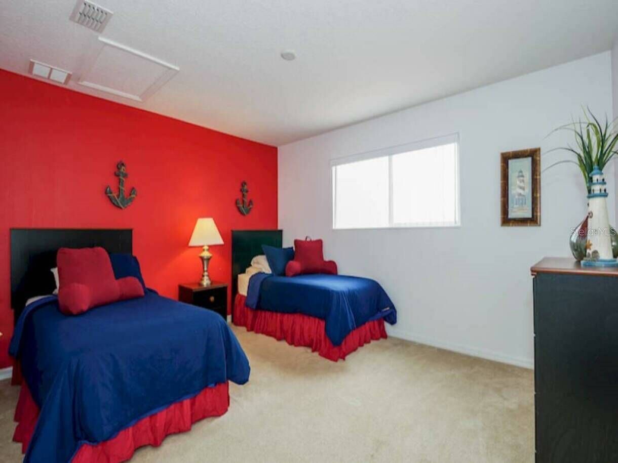 A room with two beds, a window, and a desk with a lamp.
