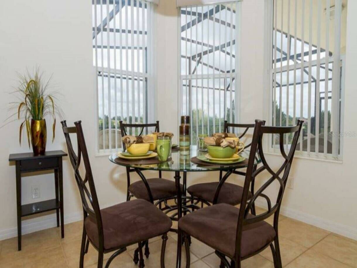 A dining area with a glass table surrounded by four chairs, a small side table with a vase, and a window with metal bars.
