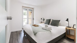 A modern bedroom with a large bed, bedside tables, a nightstand, a window, and a door. - Belem Boutique II by Homing (Lisbon)