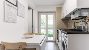 A modern kitchen with a built-in oven, a washing machine, and a dining area with a bowl on the table. - Belem Boutique III by Homing (Lisbon)