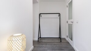 A hallway with a wooden floor, a black metal rack, and a wicker lamp. - Belem Boutique III by Homing (Lisbon)