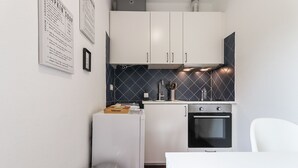 Une cuisine compacte avec des meubles blancs, un dosseret en carreaux noirs, un évier en acier inoxydable et un four encastré.