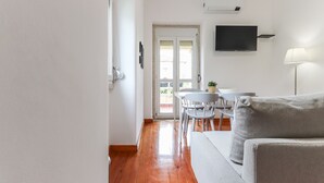 Una sala de estar moderna con un sofá, una mesa de comedor con sillas y un televisor montado en la pared.