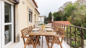 A wooden table set for four with chairs, a balcony railing, and a view of trees and buildings. - Belem Boutique IX by Homing (Lisbon)