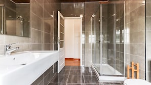 A modern bathroom with a large white bathtub, a glass-enclosed shower, and a wooden floor. - Belem Boutique IX by Homing (Lisbon)