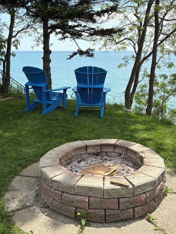 A fire pit with two Adirondack chairs and a view of the water.