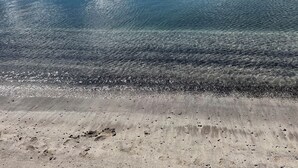 Una playa con agua cristalina y un faro distante.