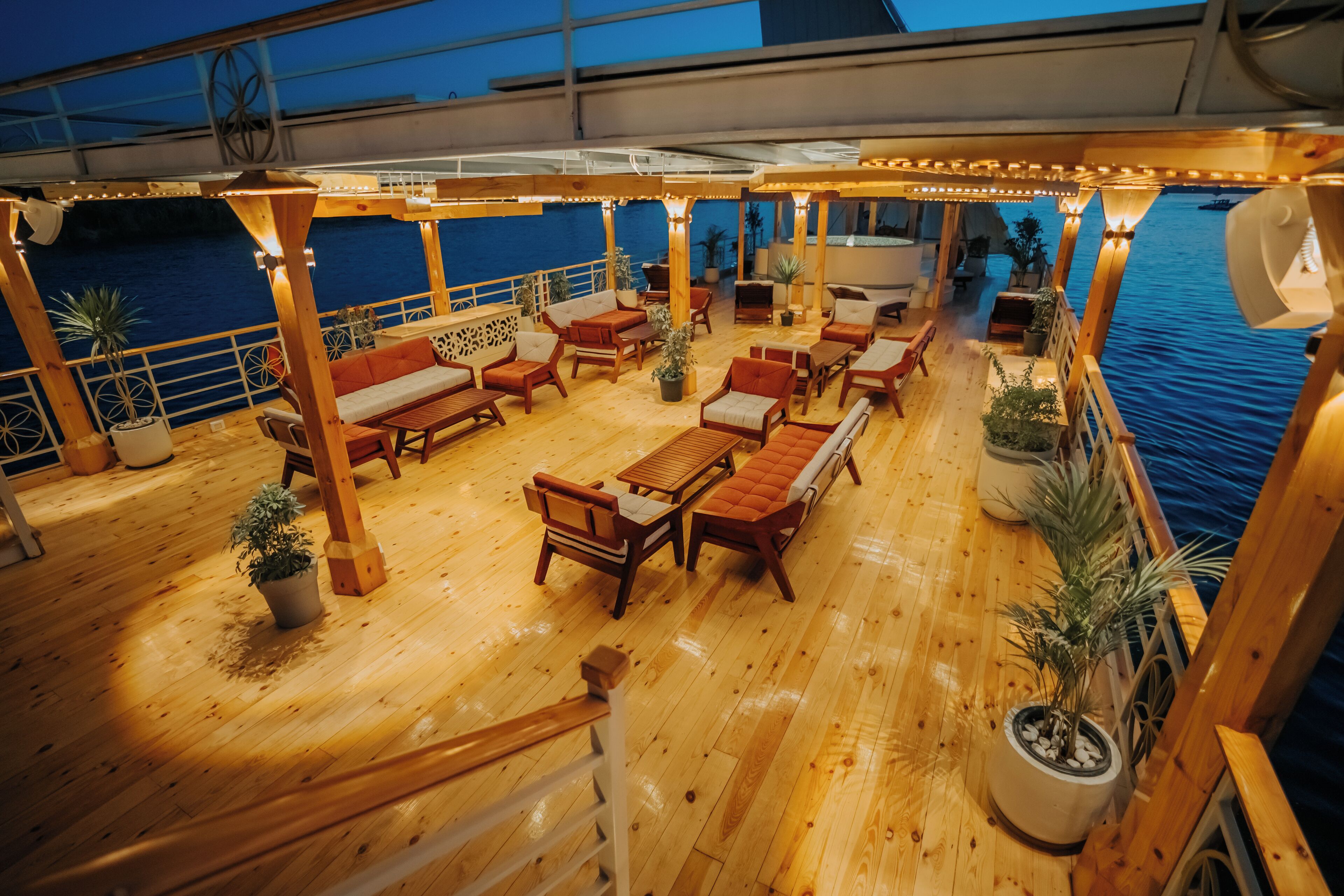 A wooden deck with outdoor seating, potted plants, and a view of the water.