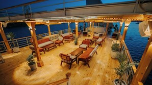 A wooden deck with outdoor seating, potted plants, and a view of the water.