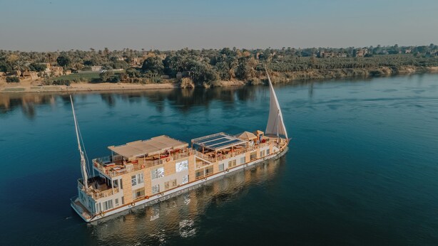 A large, multi-deck boat with a flat roof and a single mast, floating on calm water.