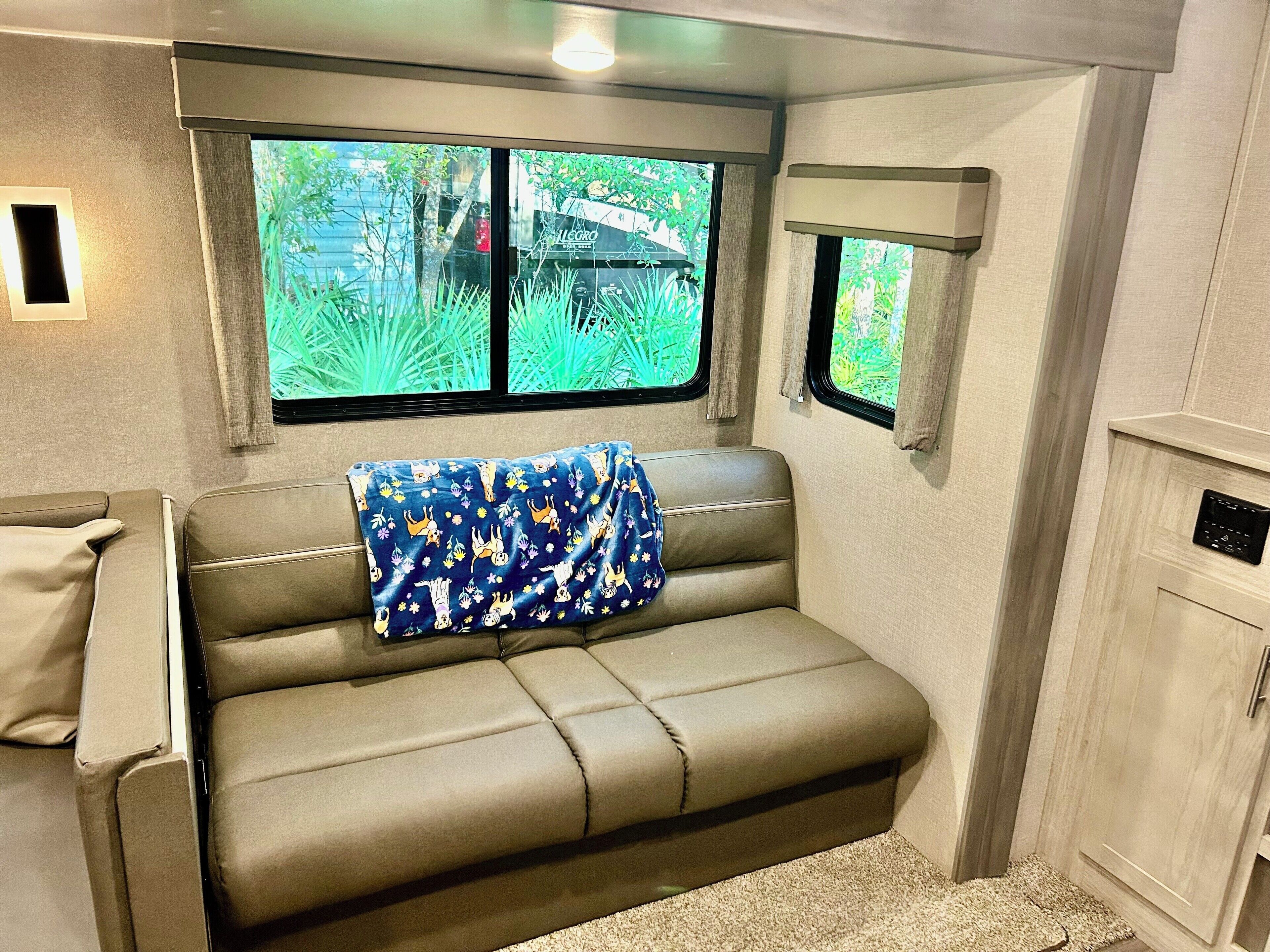Un intérieur de camping-car accueillant, avec un canapé, une fenêtre donnant sur un paysage verdoyant et un petit placard.