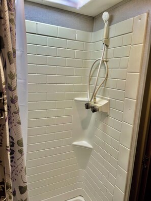 Une douche d’angle avec des murs recouverts de carreaux blancs, une douchette à main et un robinet fixé au mur.