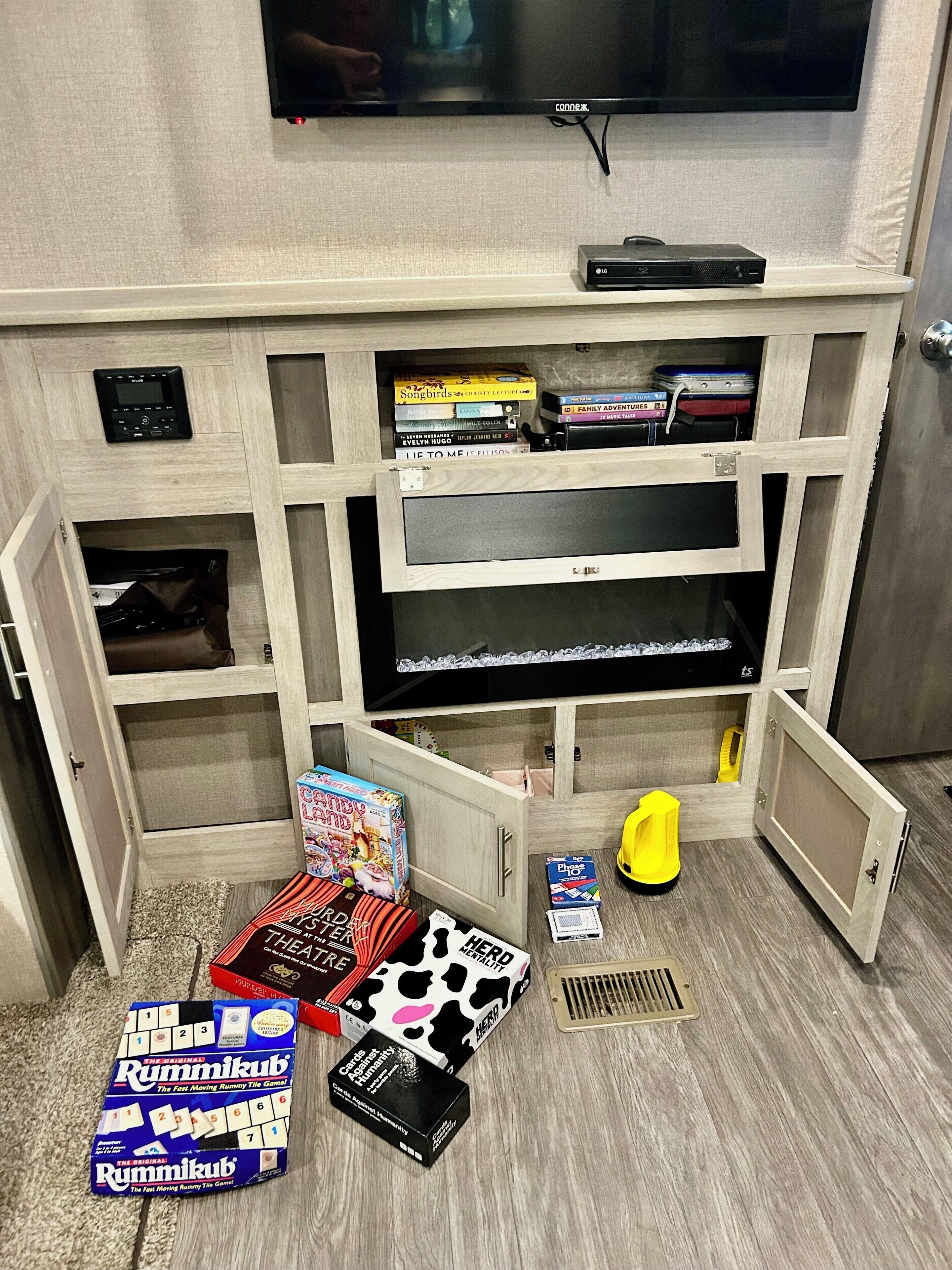 A room with a television mounted on the wall, a wooden entertainment unit with shelves, and a variety of board games on the floor.
