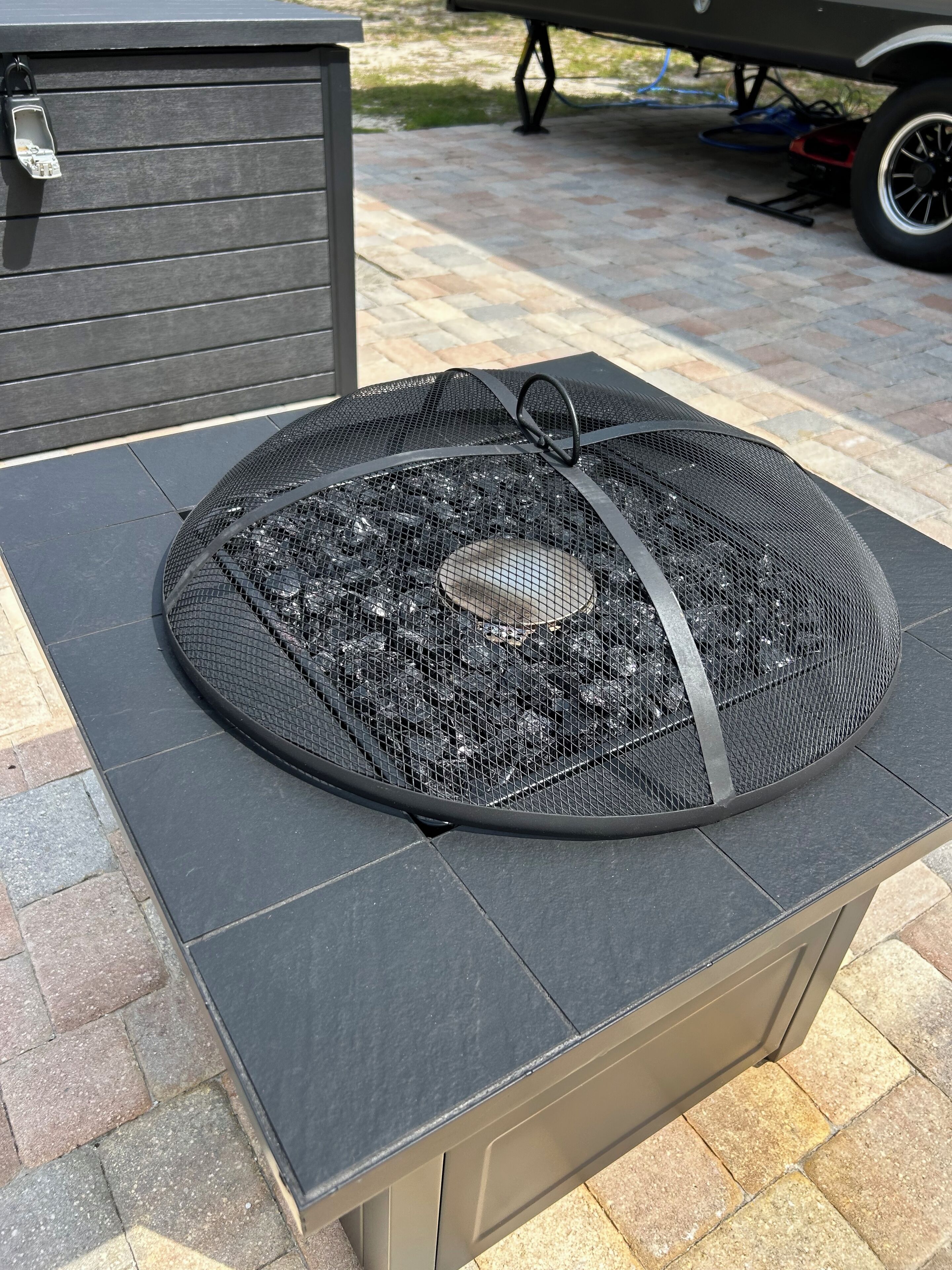 Een ronde barbecue voor buiten met een metalen rooster en een handvat, geplaatst op een grijze buitentafel.