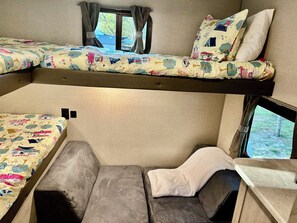 Un intérieur de camping-car compact comprenant un lit superposé, un coin salon et une fenêtre offrant une vue sur l’extérieur.