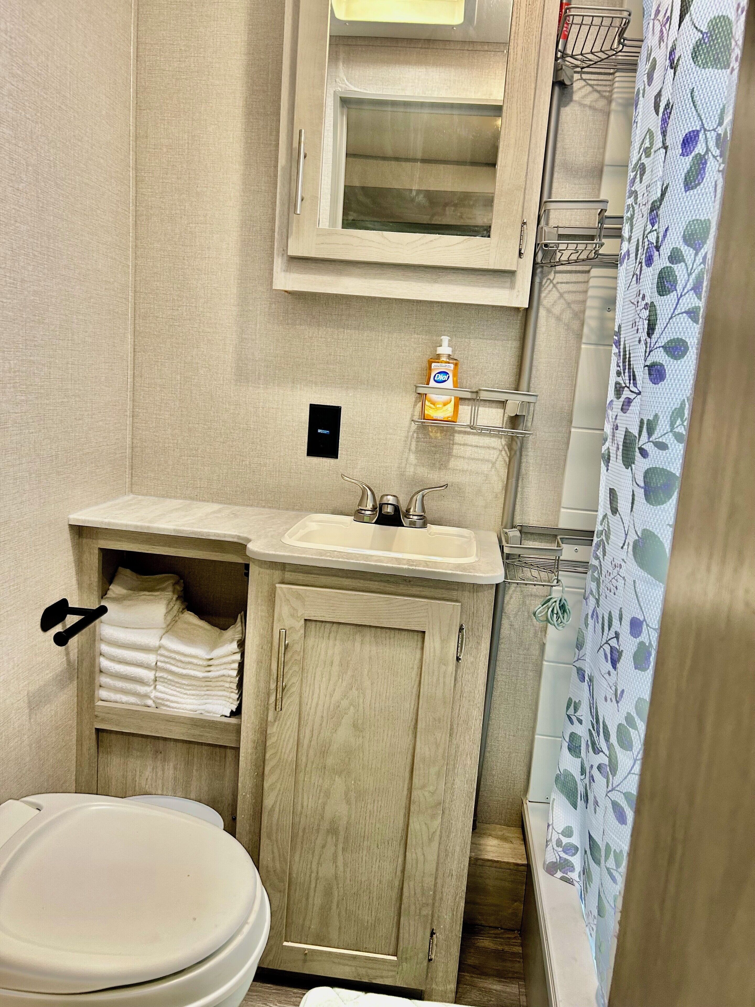 Ein Badezimmer mit Toilette, Waschbecken und einem Holzschrank. Auf der Ablage über dem Waschbecken steht eine Handseifenflasche.