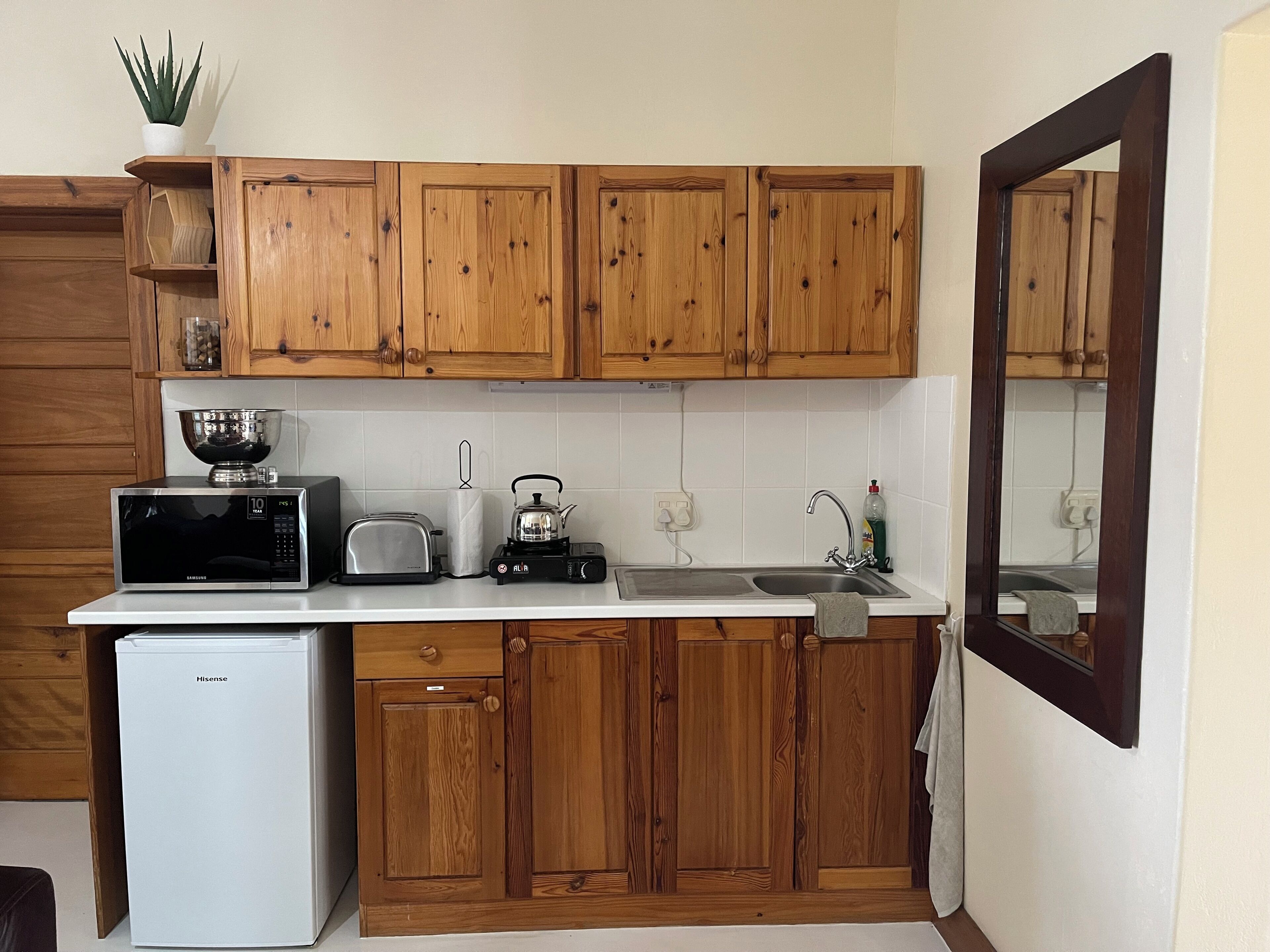 A compact kitchen with wooden cabinets, a microwave, a toaster, a kettle, and a sink.