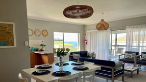 A modern living room with a dining area, featuring a sofa set, a coffee table, and a dining table with placemats. - Footprints in Kleinmond (Kleinmond)