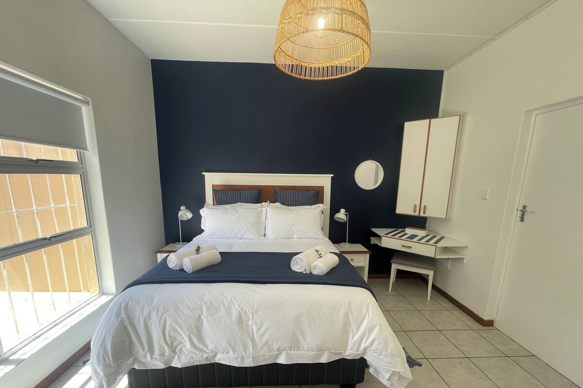 A neatly arranged bedroom with a bed, bedside tables, a desk, and a wardrobe.