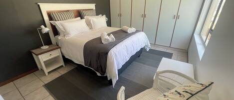 A neatly arranged bedroom with a bed, bedside table, chair, wardrobe, and a window.
