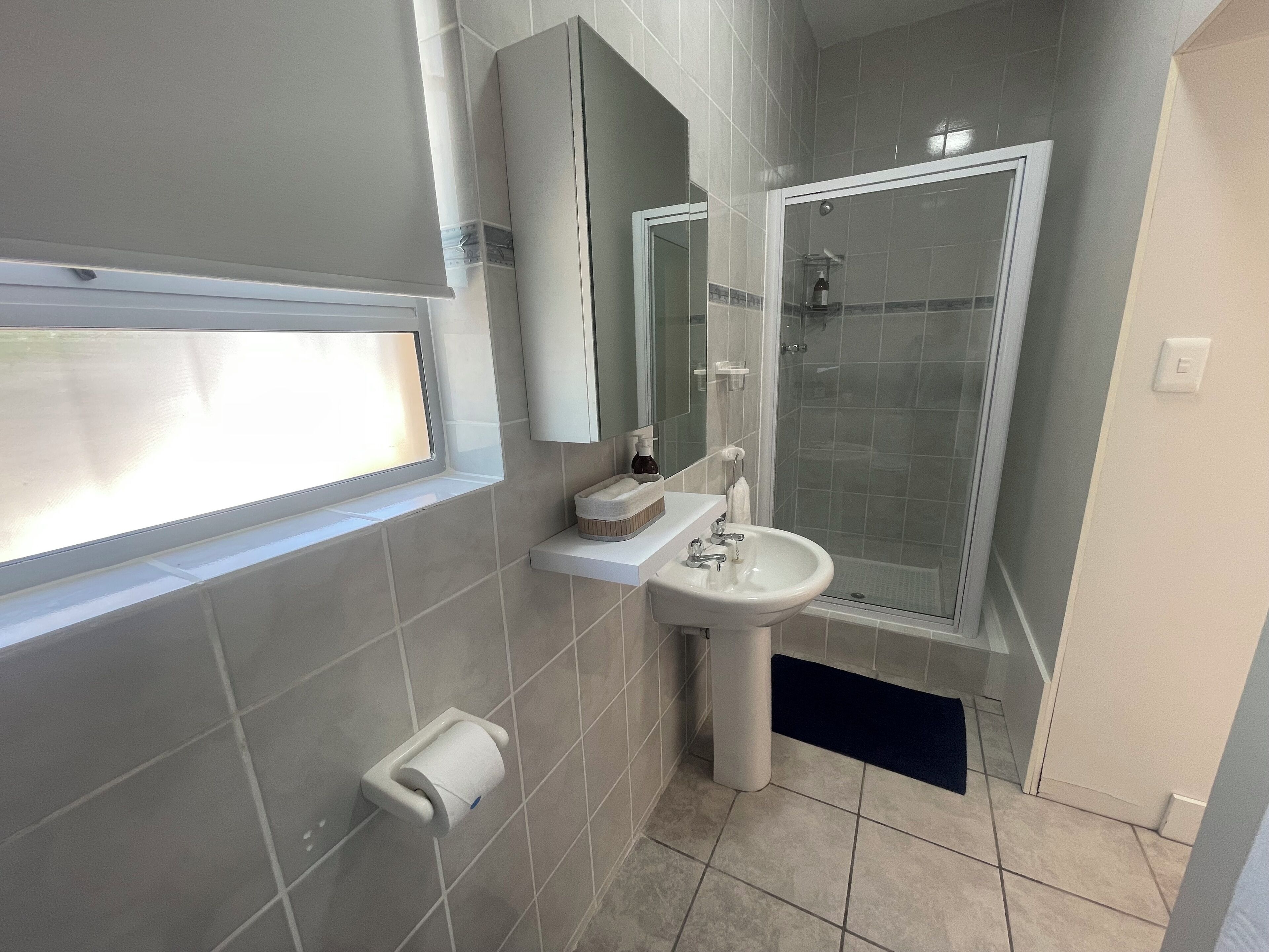 Un baño con ventana, lavamanos, espejo y ducha.