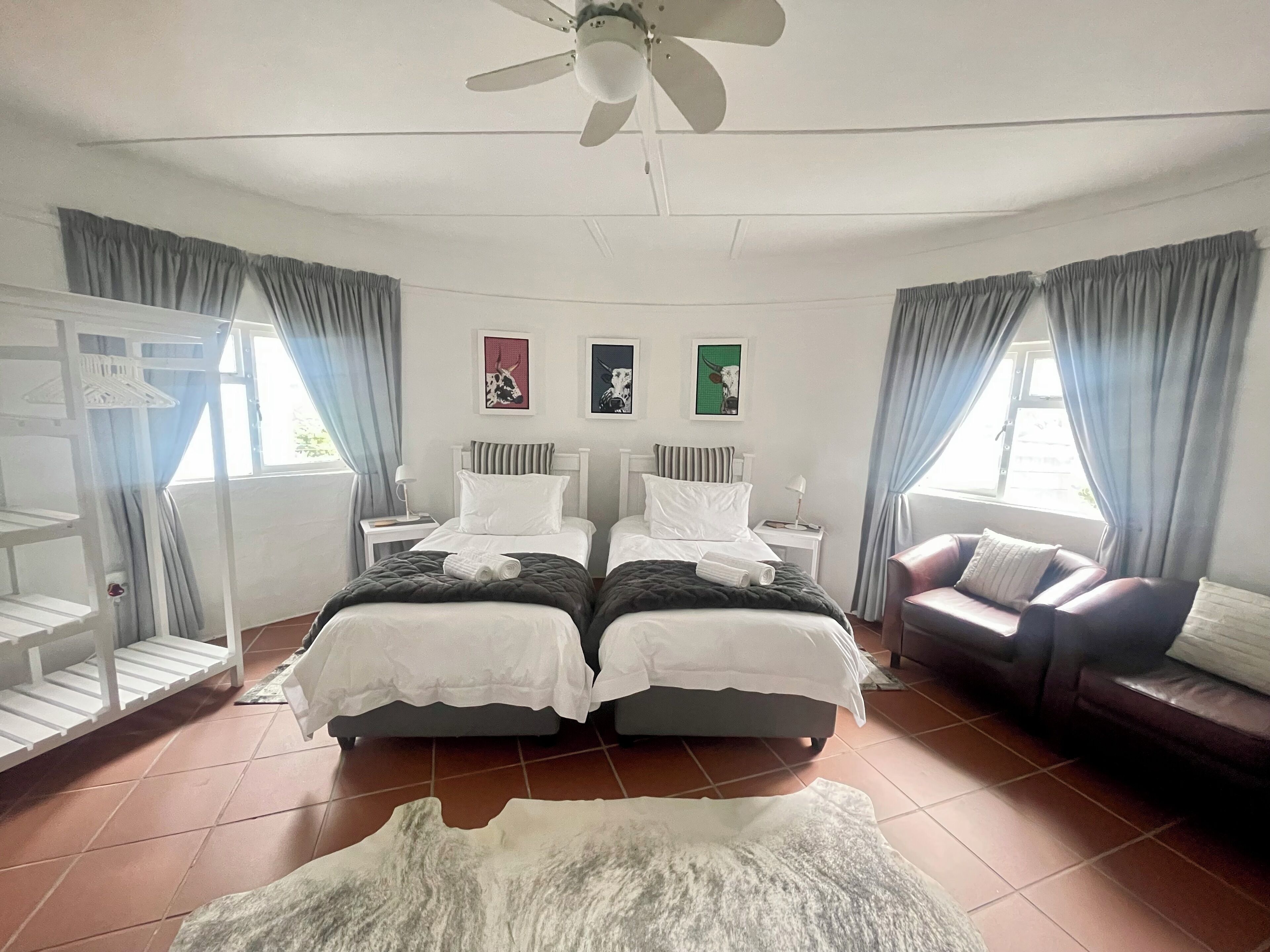 A hotel room with two beds, a ceiling fan, a sofa, and artwork on the walls.