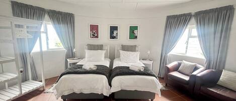 Une chambre d’hôtel avec deux lits, un ventilateur de plafond, un canapé et des œuvres d’art accrochées aux murs.